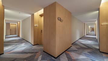 Pasillo de hotel con puertas de madera, placas con números de habitación y alfombra estampada.