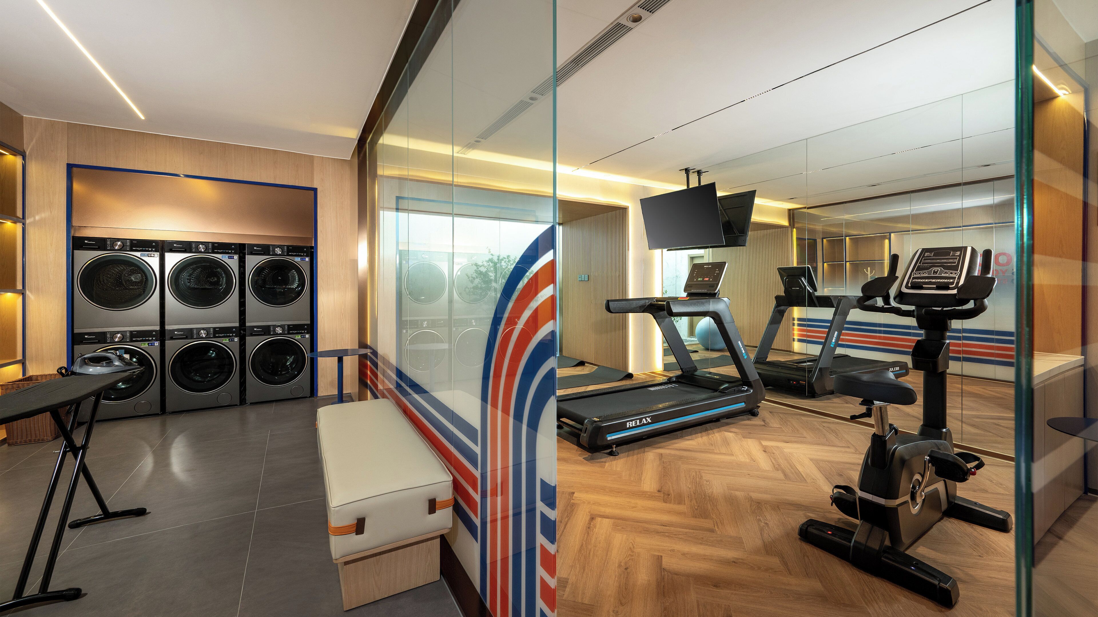A hotel room with a gym area including a treadmill, stationary bike, and a washing machine.