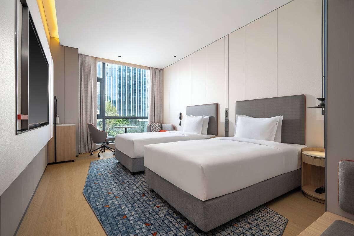 A hotel room with two beds, a desk, a chair, a small table, and a window with curtains.