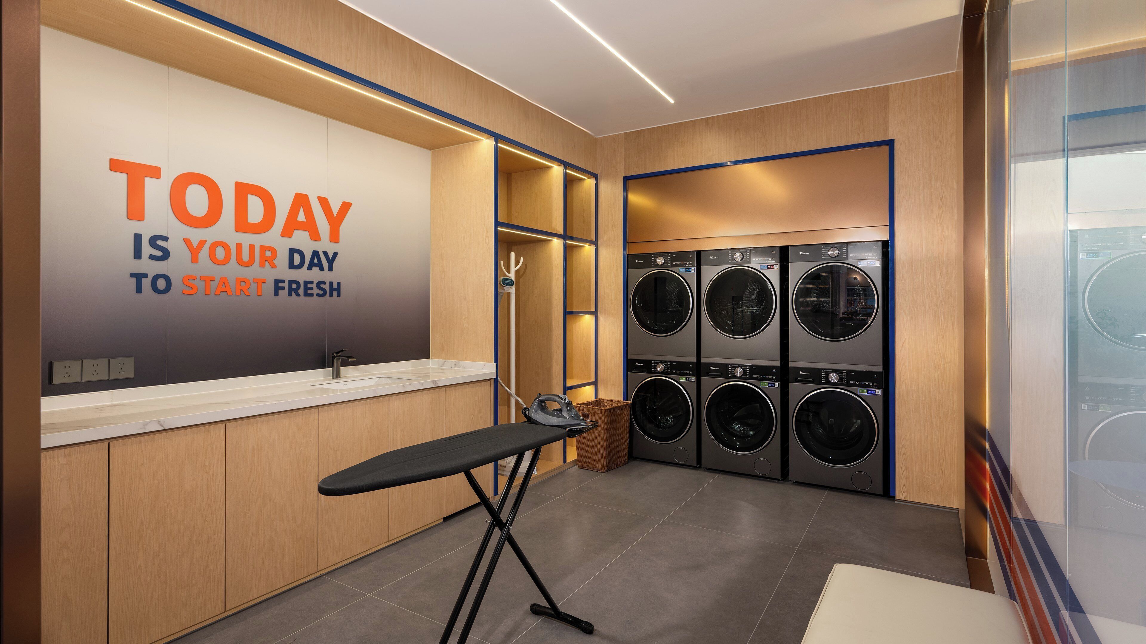 A modern laundry facility with a motivational wall, multiple washing machines, and a foldable ironing station.