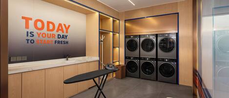 A modern laundry facility with a motivational wall, multiple washing machines, and a foldable ironing station.