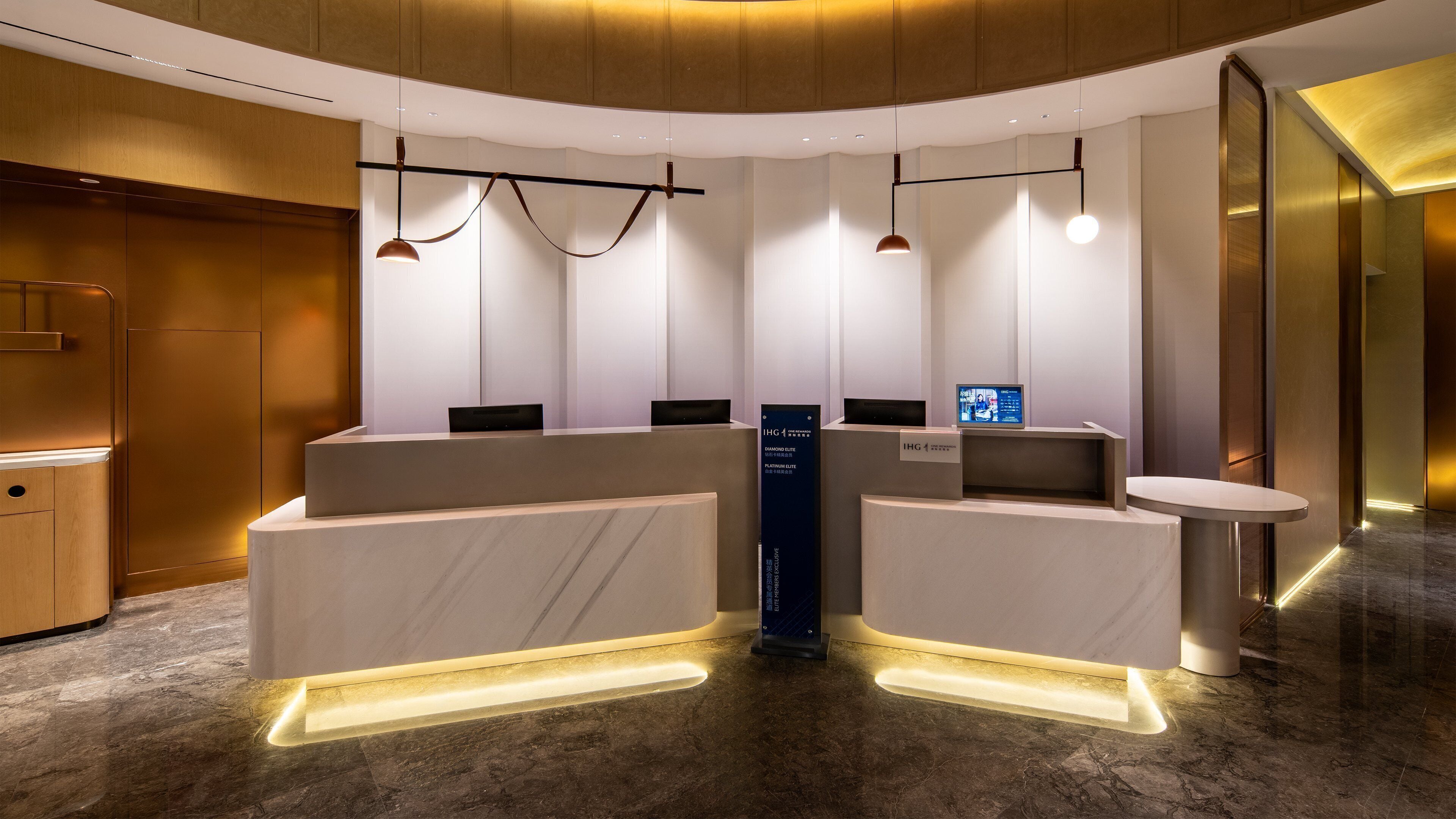 A modern reception desk with a digital screen, marble flooring, and pendant lighting.