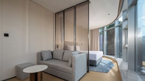 A modern hotel room with a grey sofa, a small round table, and a large window offering a view of greenery. - Holiday Inn Express Shenzhen Sports Center by IHG (Shenzhen)