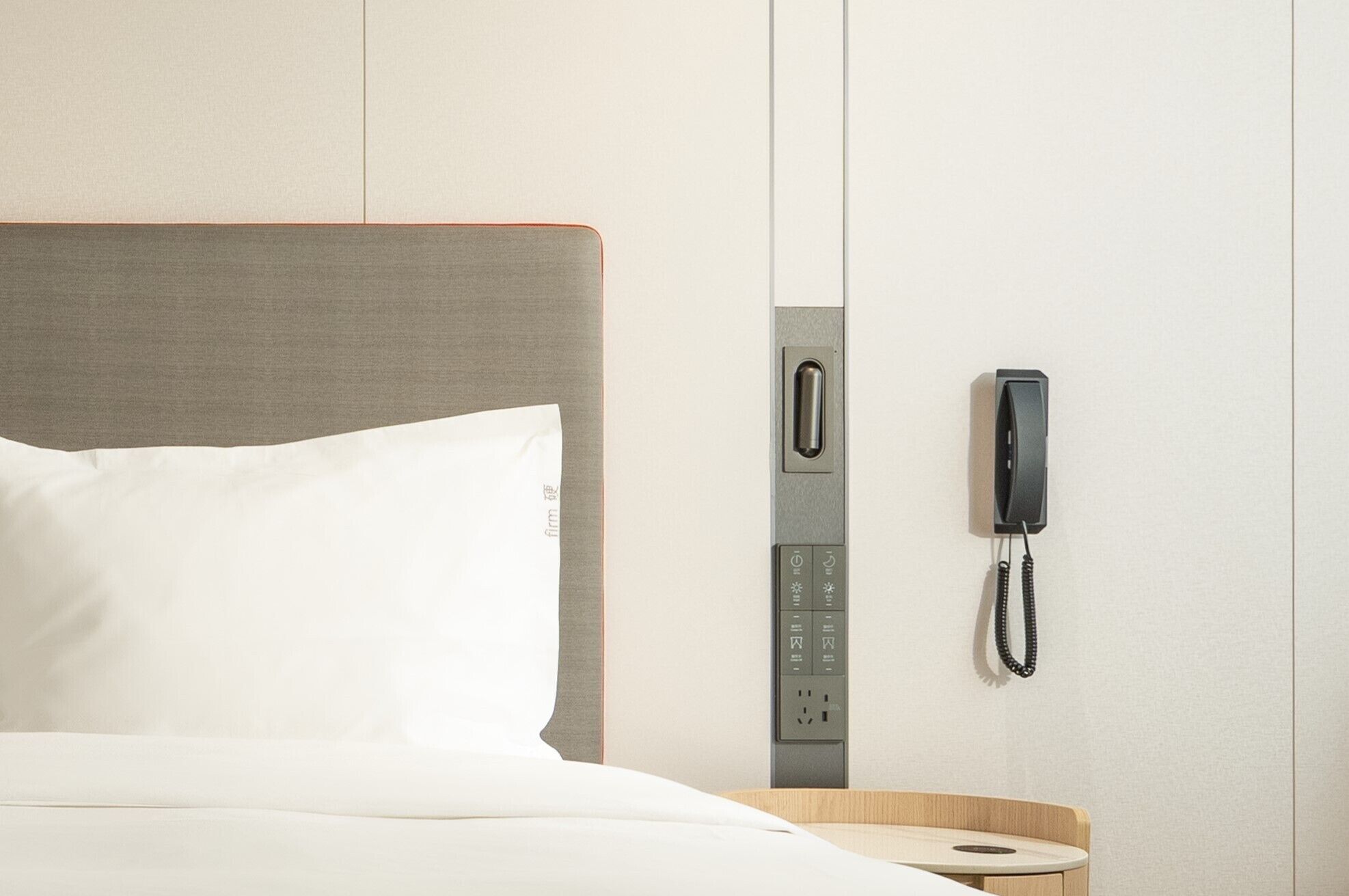 A hotel room with a bed, a bedside table, a telephone, and a power outlet.