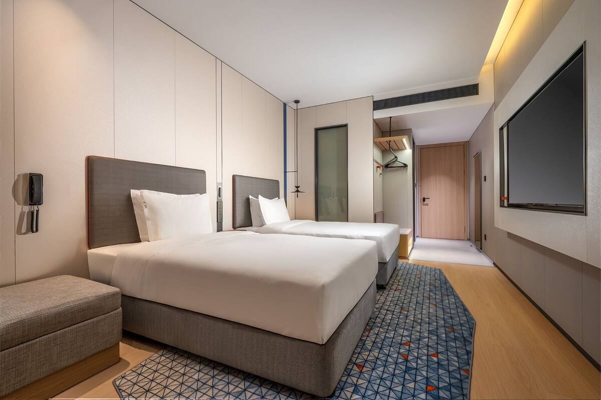A modern hotel room with two beds, a desk, a phone, and a TV.