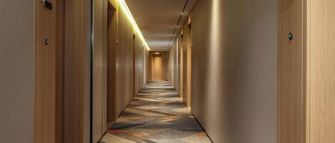 A long, narrow hallway with wooden walls and doors, carpeted with a geometric pattern.