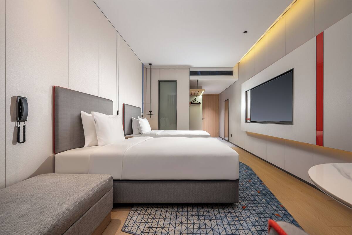 A modern hotel room with a large bed, bedside tables, a desk, a telephone, a mirror, and a TV.