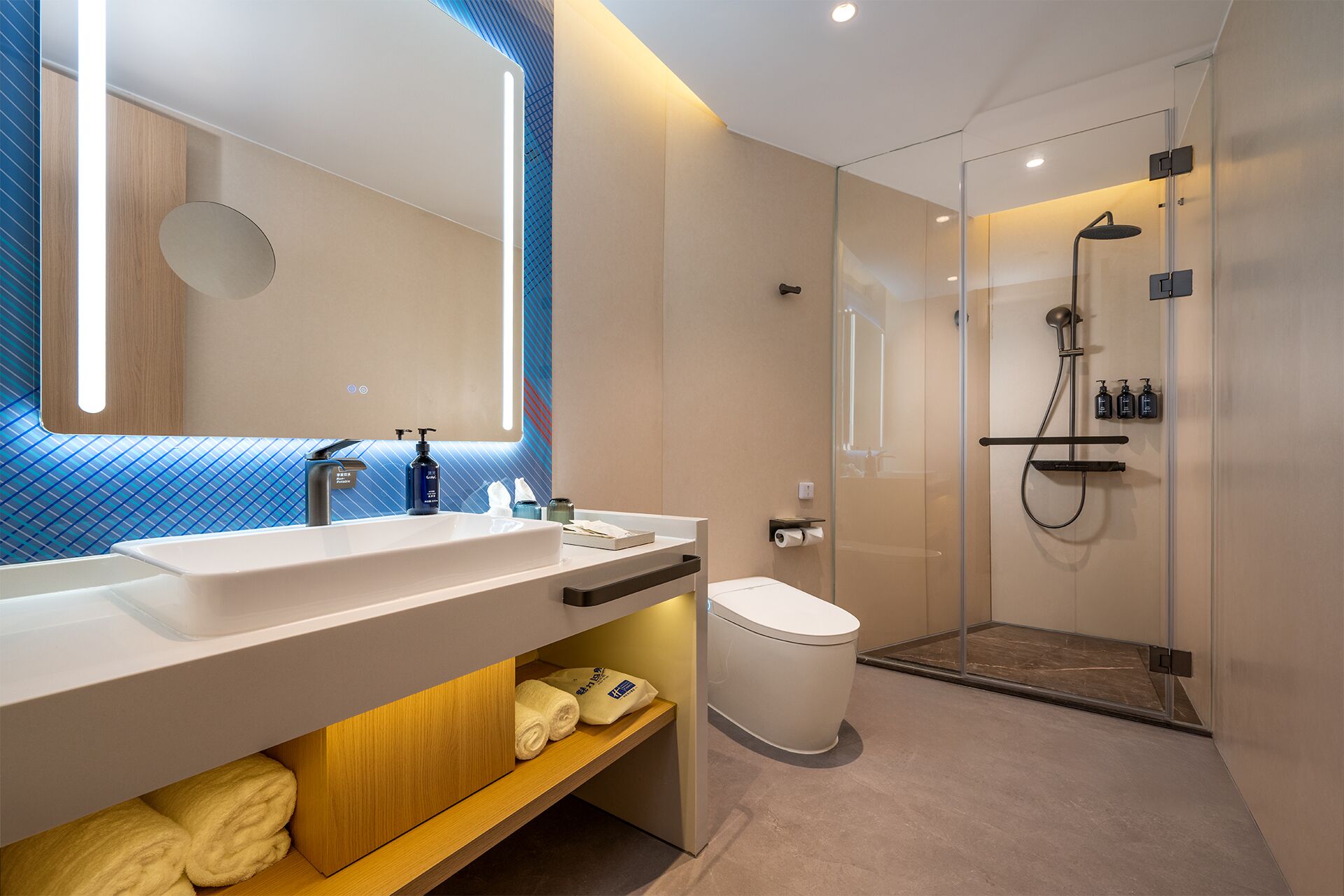 A modern bathroom with a large mirror, dual sinks, a toilet, and a glass-enclosed shower area.