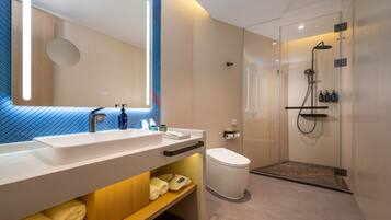 Un baño moderno con un espejo grande, lavamanos dobles, inodoro y zona de ducha con mampara de cristal.