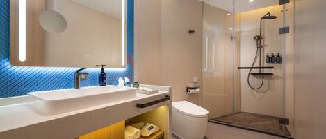A modern bathroom with a large mirror, dual sinks, a toilet, and a glass-enclosed shower area.