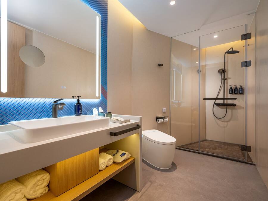 Un baño moderno con un espejo grande, lavamanos dobles, inodoro y zona de ducha con mampara de cristal.