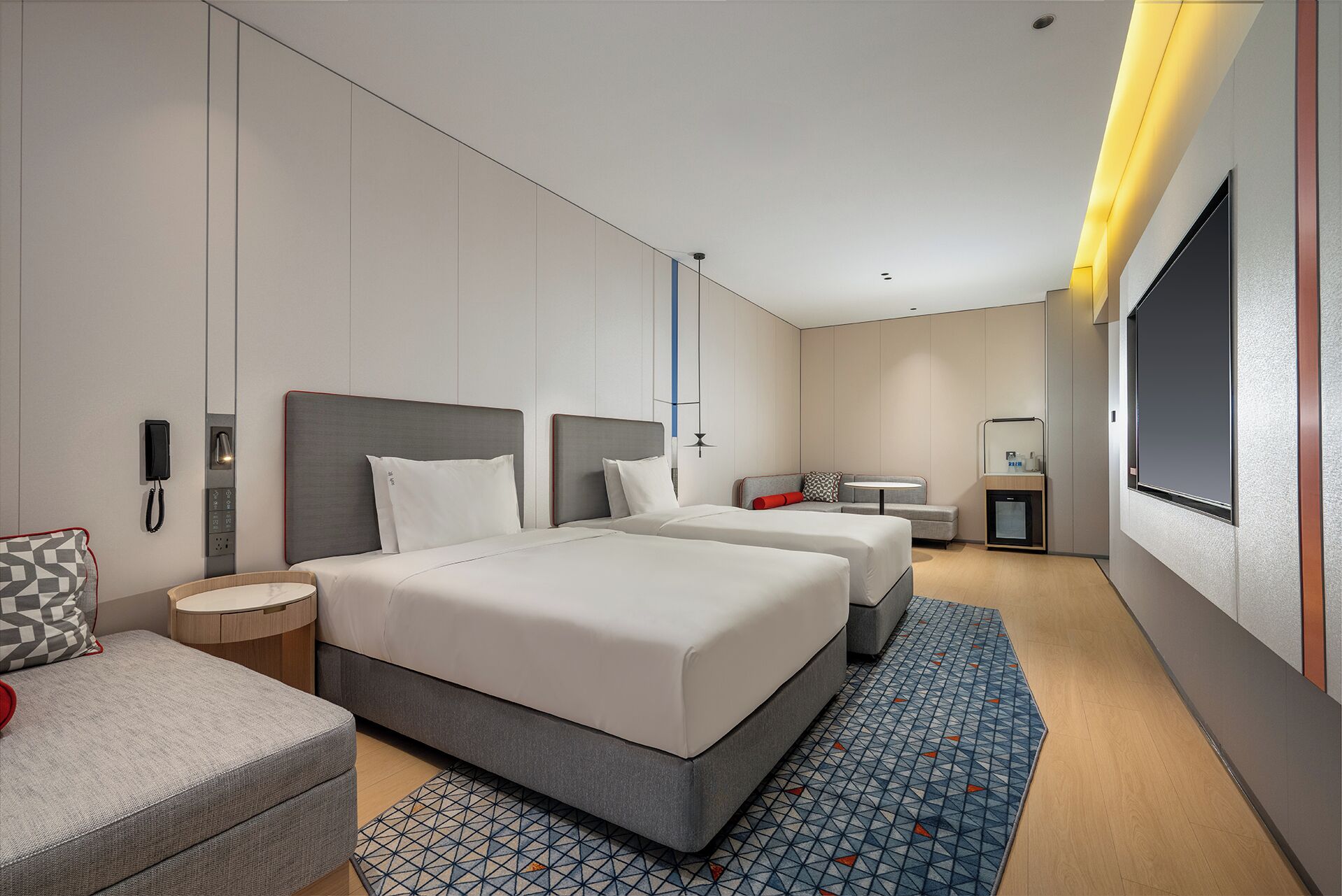 Een moderne hotelkamer met twee bedden, een bank, een kleine tafel, een bureau en een televisie.