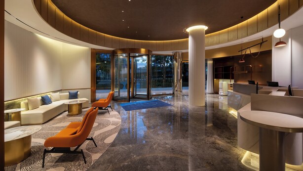 A modern lobby with a curved ceiling, seating areas, a reception desk, and glass doors leading outside. - Holiday Inn Express Shenzhen Sports Center by IHG (Shenzhen)