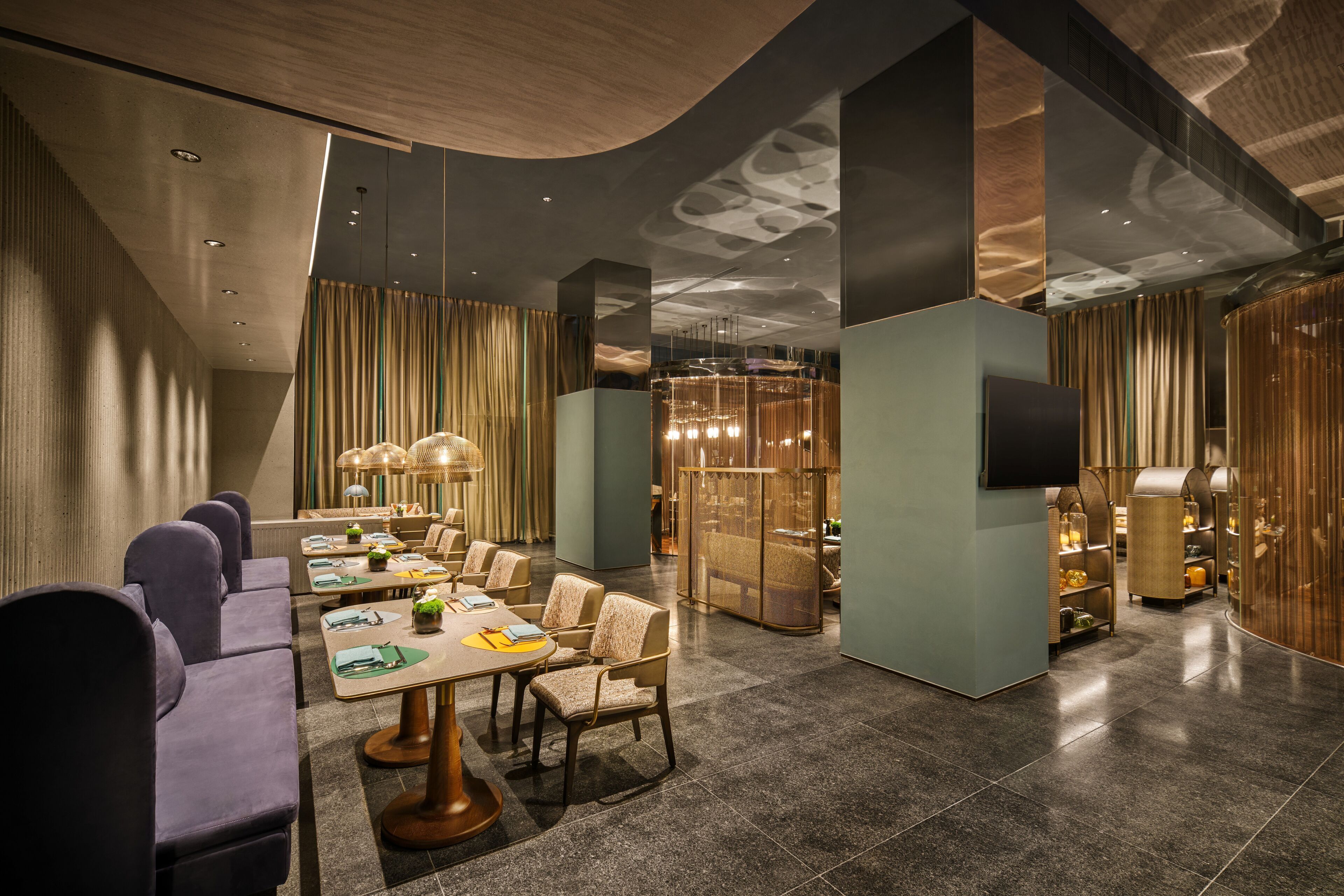 Un hall d’hôtel moderne doté d’un plafond incurvé, de coins salon et d’un écran de télévision.