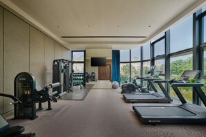 Une salle de sport moderne équipée de tapis de course, d’appareils de musculation et d’un écran de télévision.