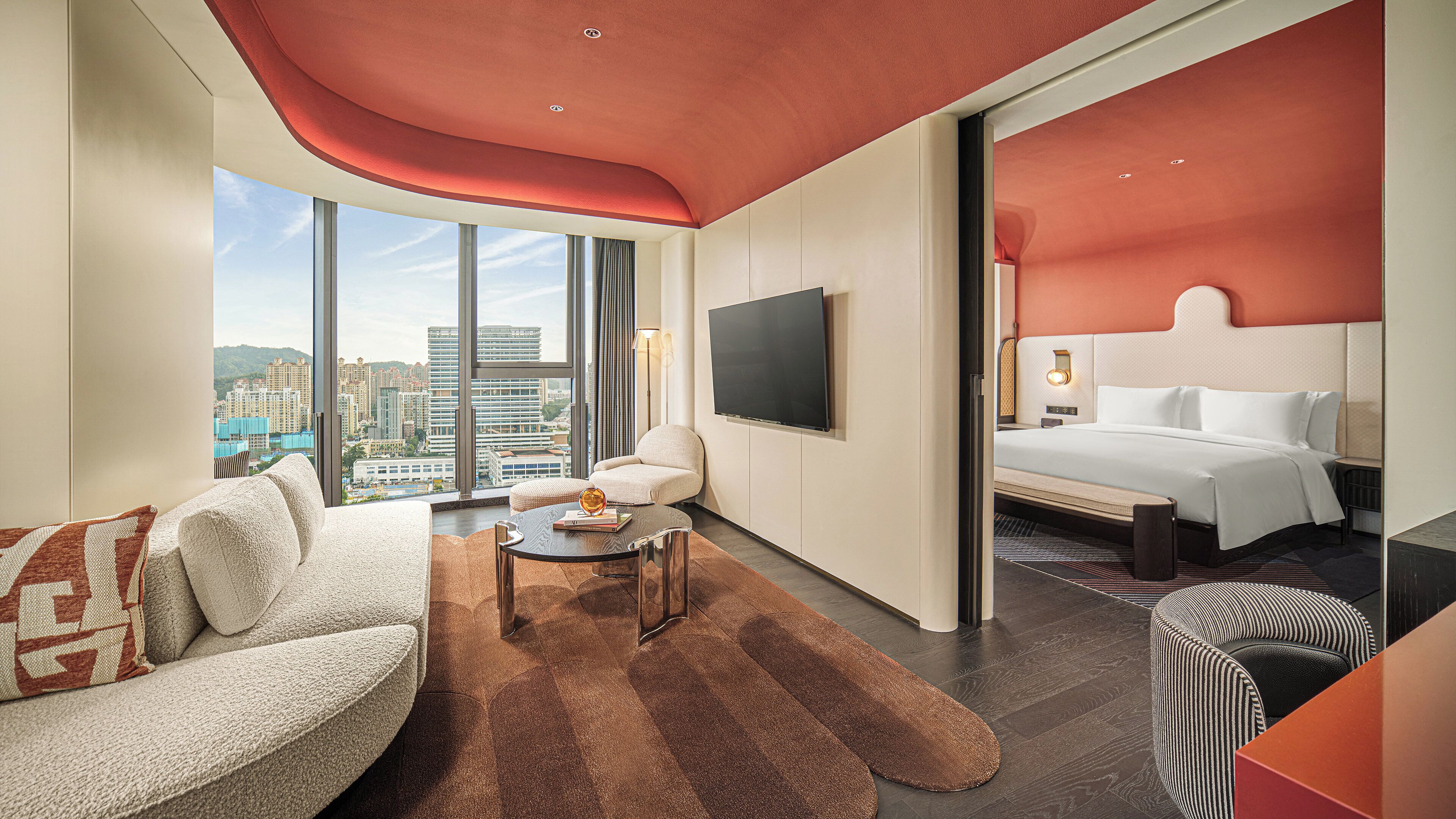 A modern hotel room with a large bed, a sofa, a coffee table, and a TV.