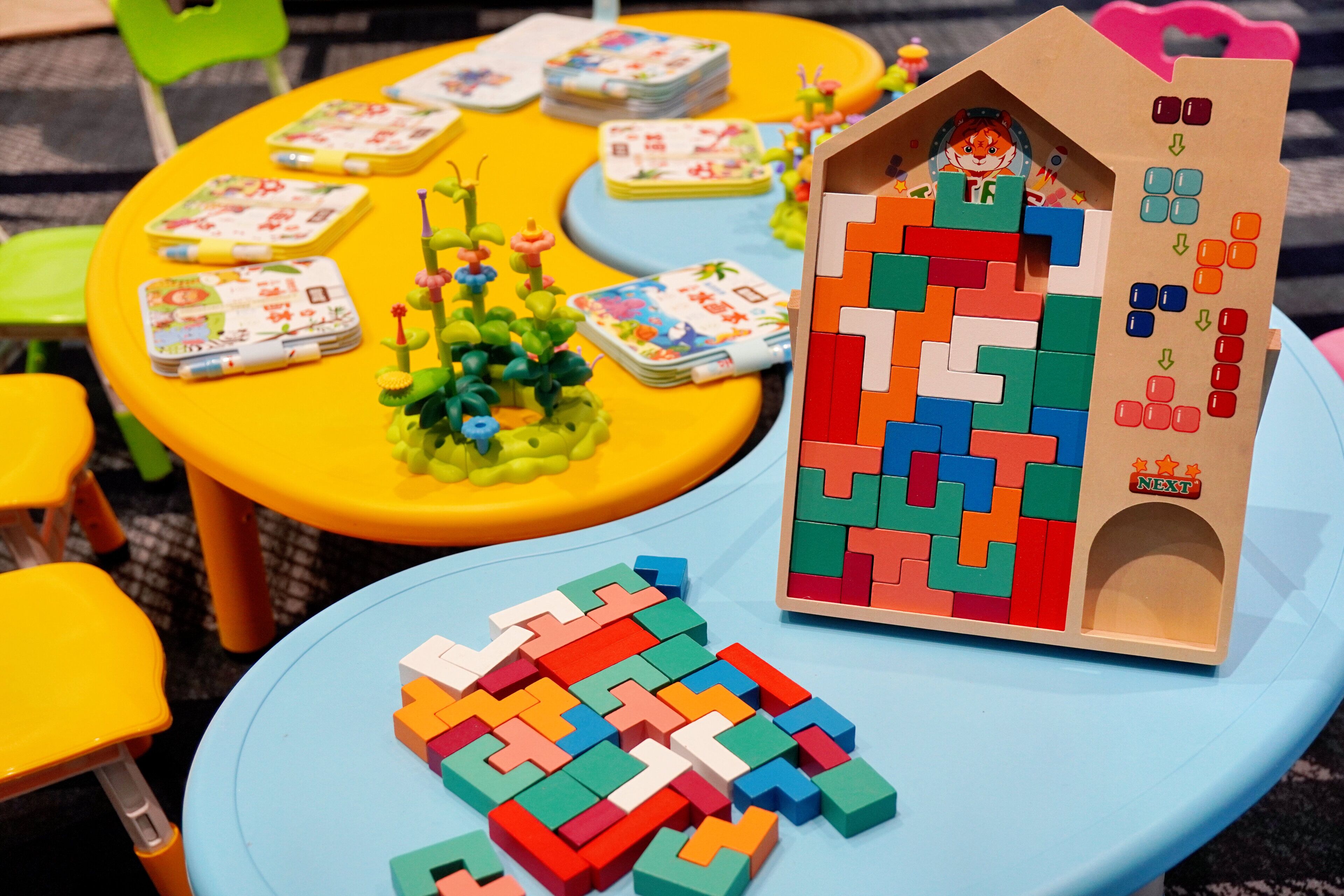 A children's play area with colorful tables, a toy house, and building blocks.