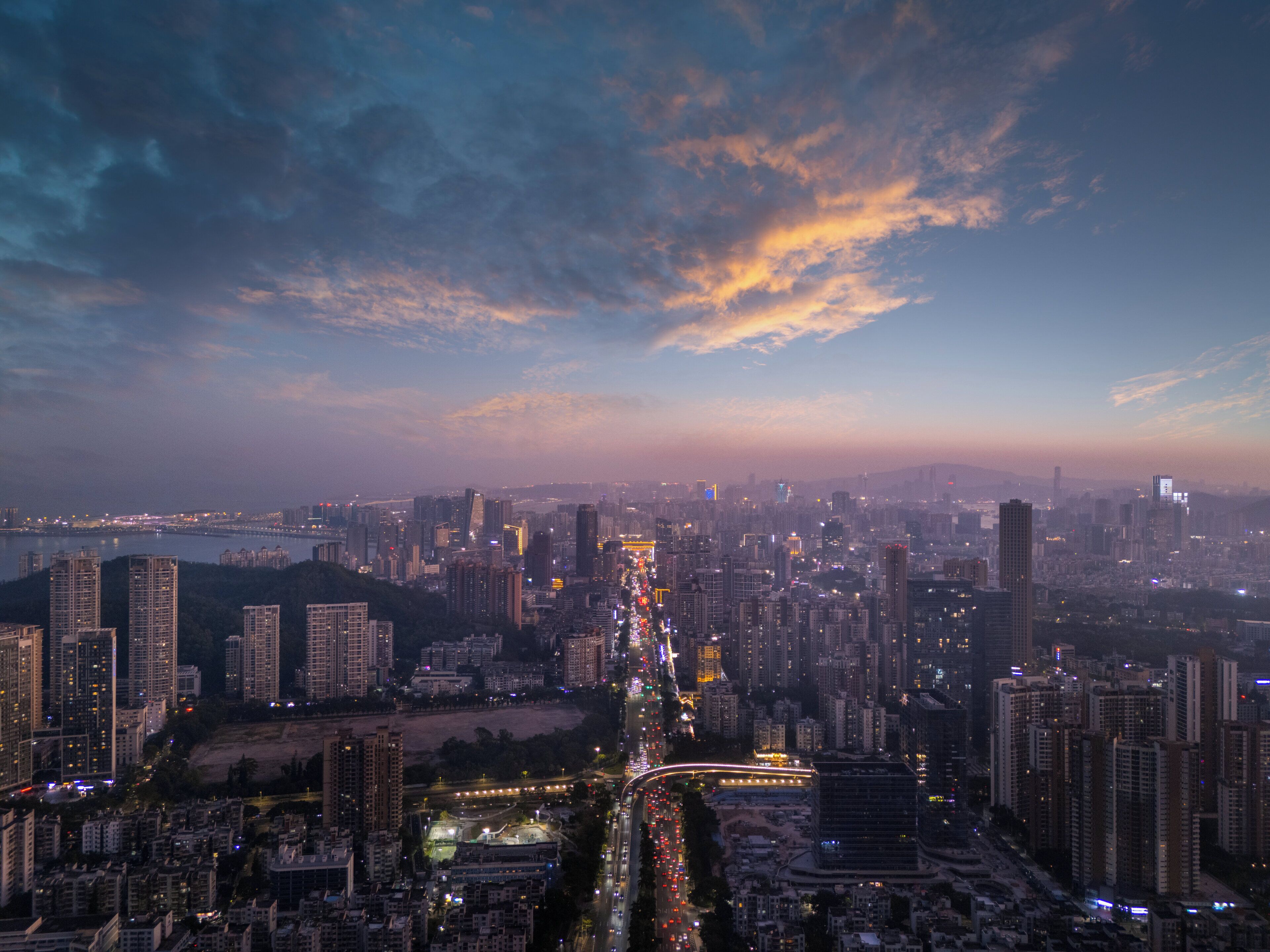 A cityscape with a dense cluster of high-rise buildings, a prominent highway, and a river in the foreground.