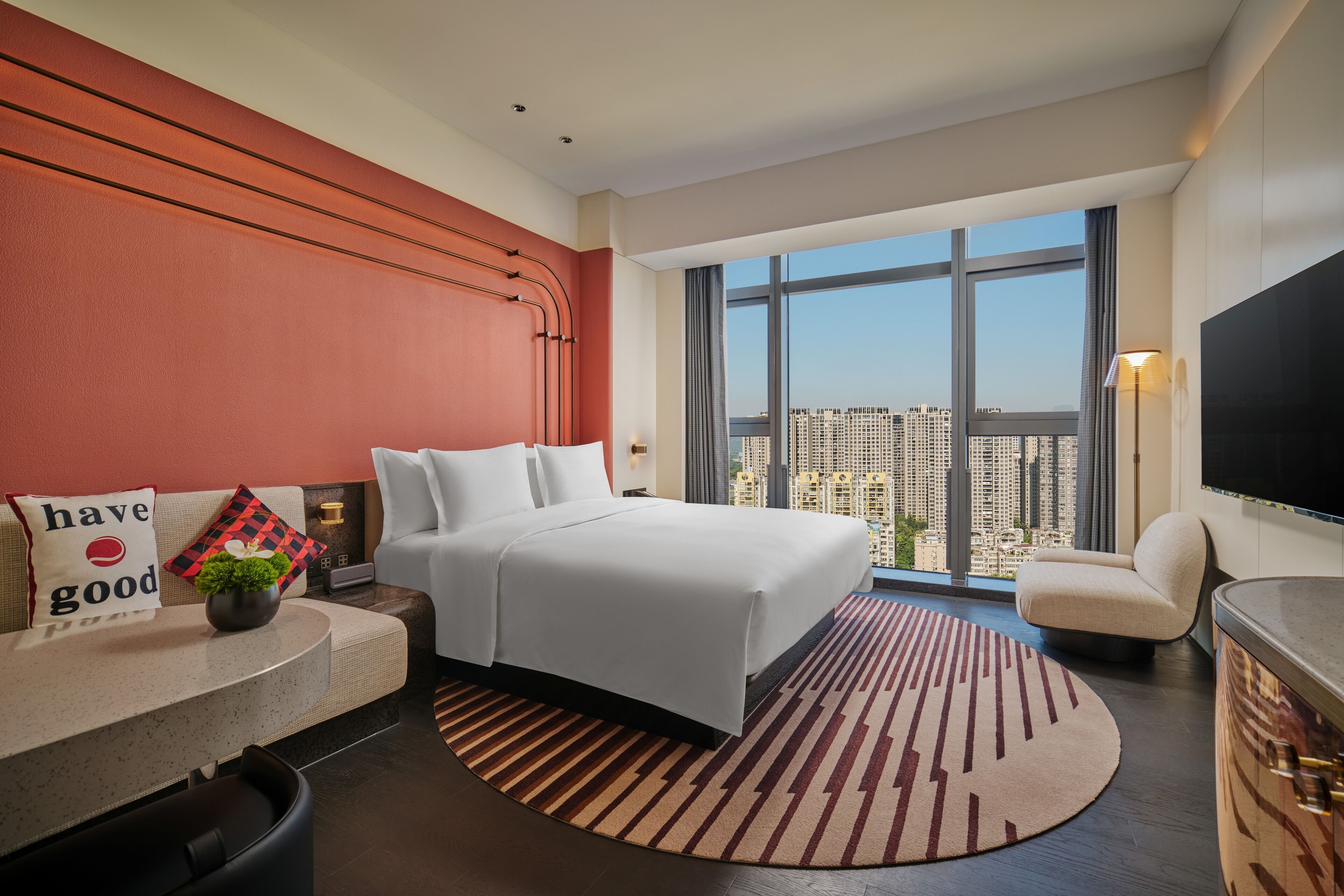 Une chambre d’hôtel moderne avec un grand lit, un canapé, une télévision et une vue sur la ville.