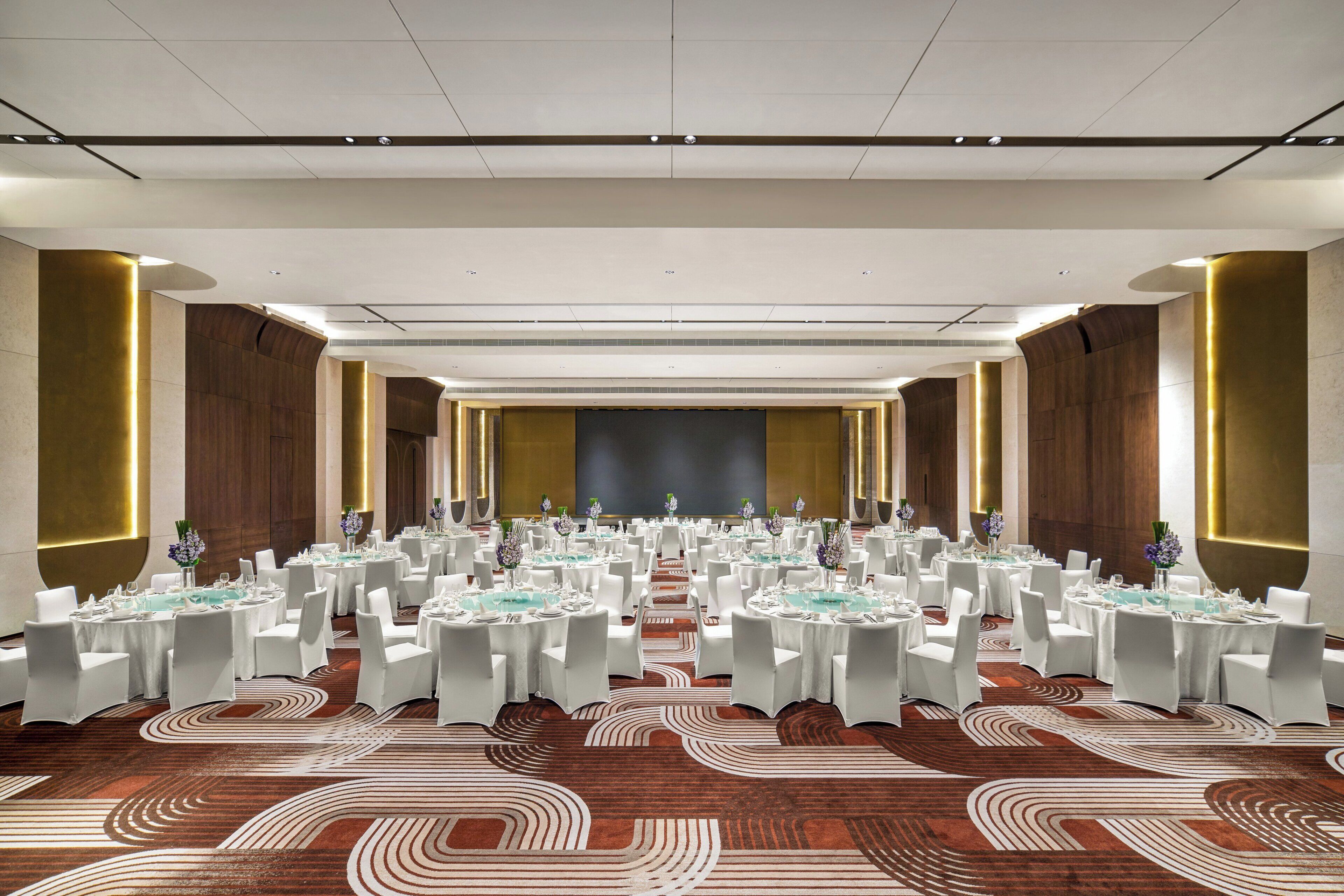 A large conference room with round tables, white chairs, and a stage at the front.