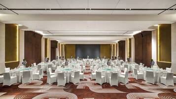 A large conference room with round tables, white chairs, and a stage at the front.