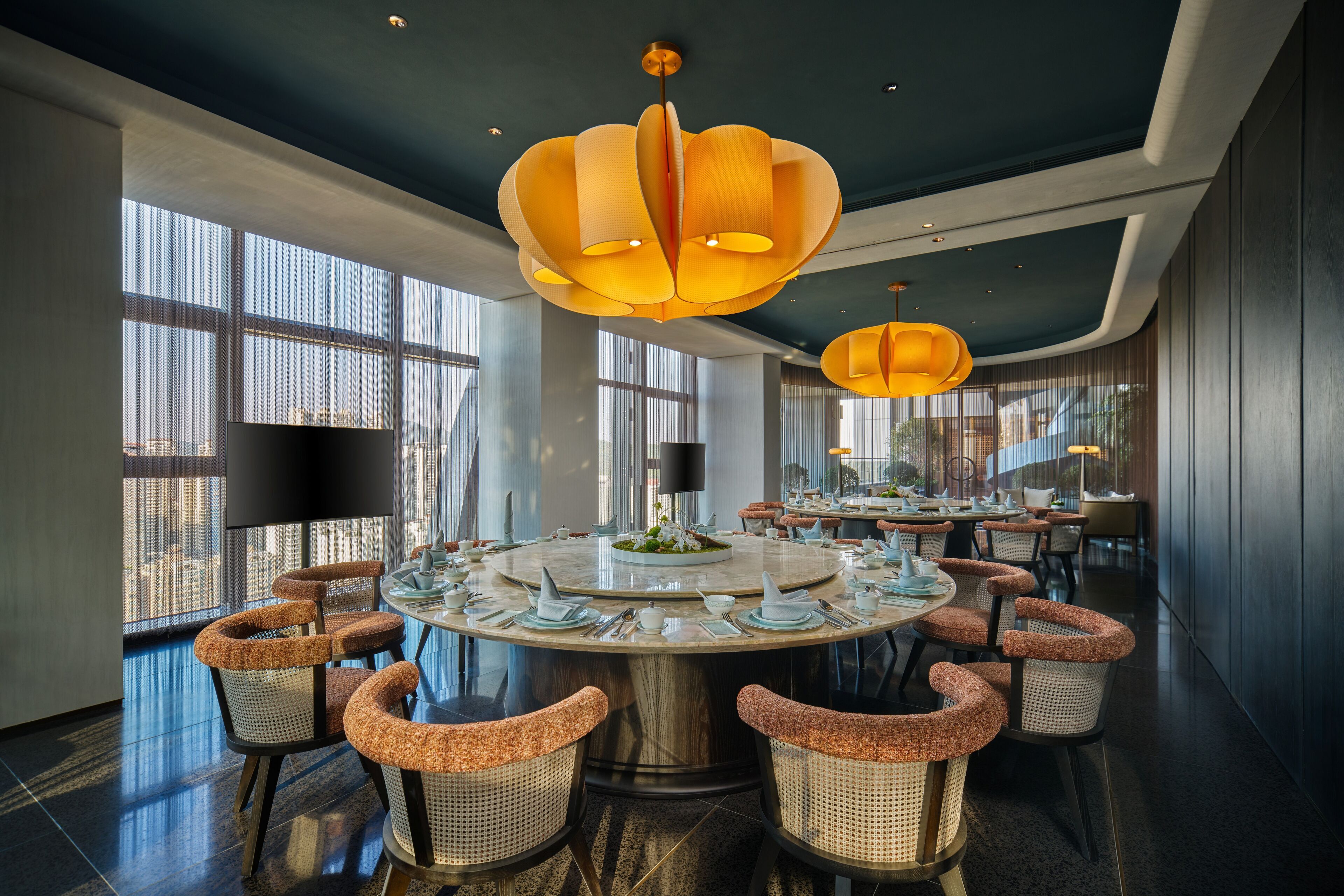Un espace de salle à manger moderne avec une table ronde, des chaises en osier et des luminaires suspendus.