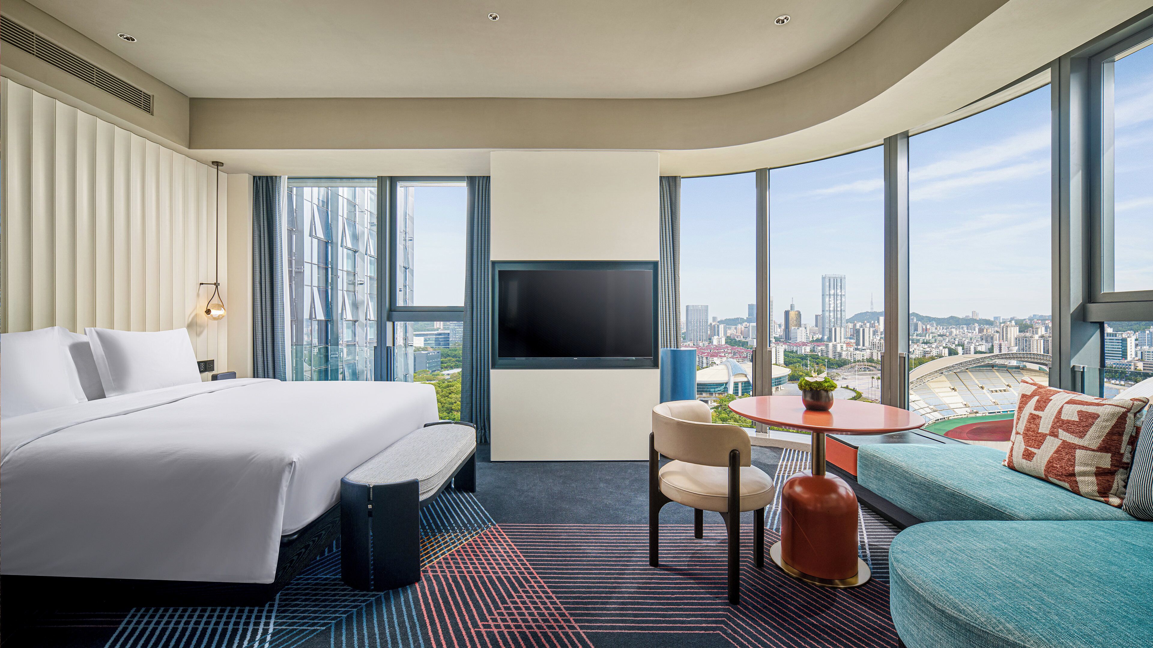 A hotel room with a bed, a seating area, a TV, and a city view.