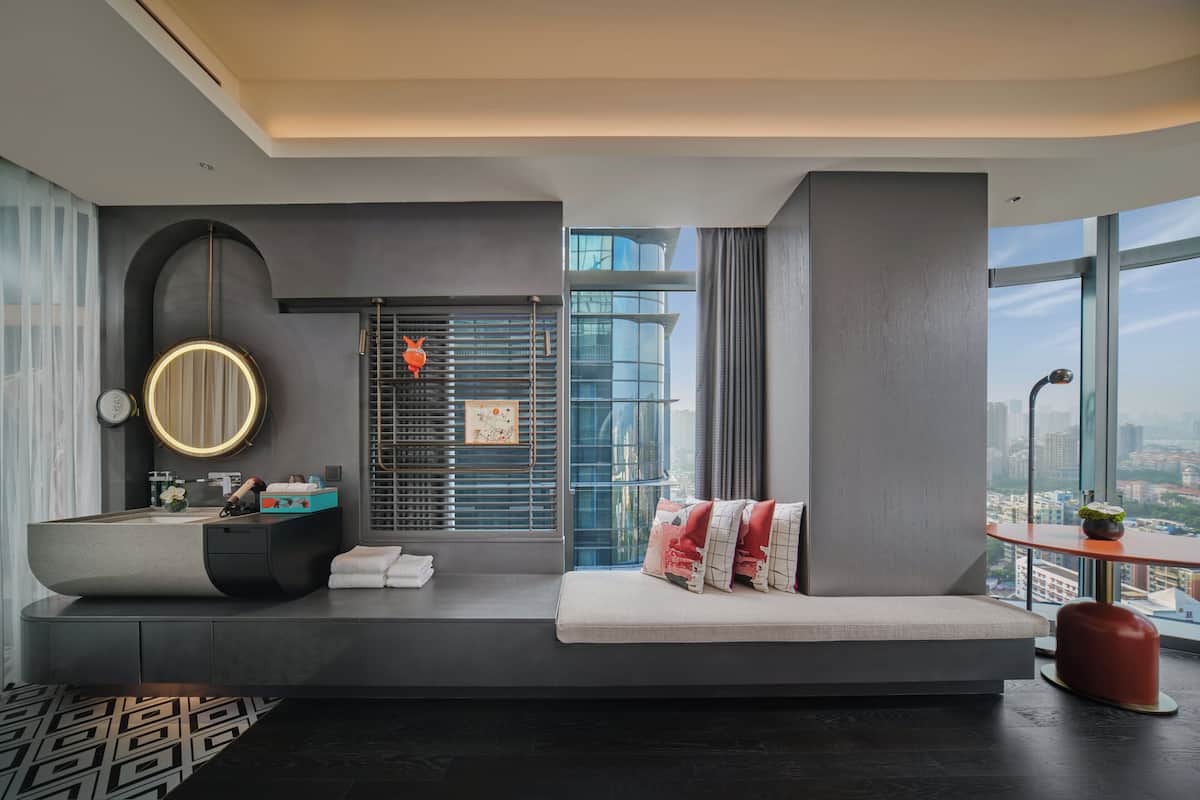 A modern bathroom with a large mirror, a round sink, and a bench with pillows.