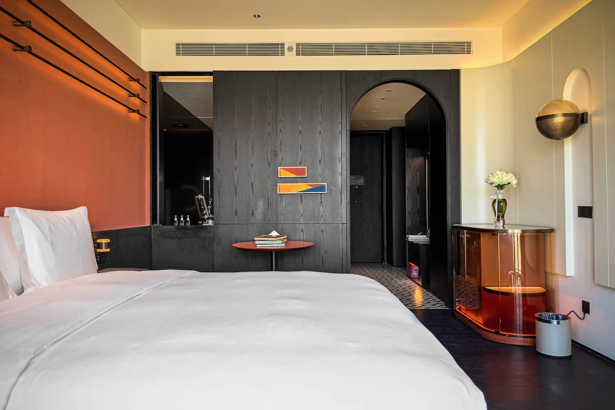 A modern hotel room with a large bed, a small round table, and a unique cylindrical side table.
