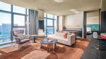 Una habitación de hotel moderna con un ventanal grande, un sofá, una silla, una mesita de centro y una zona de cocina.