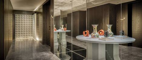 Una hall d'hotel moderna con pavimenti riflettenti, rivestimenti in legno scuro e un tavolo rotondo centrale con oggetti decorativi.