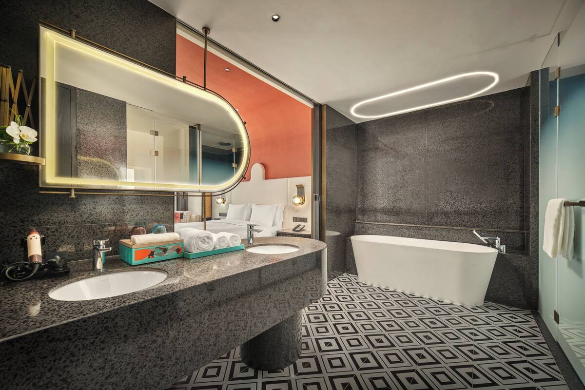 A modern bathroom with two sinks, a large mirror, a bathtub, and patterned floor tiles.
