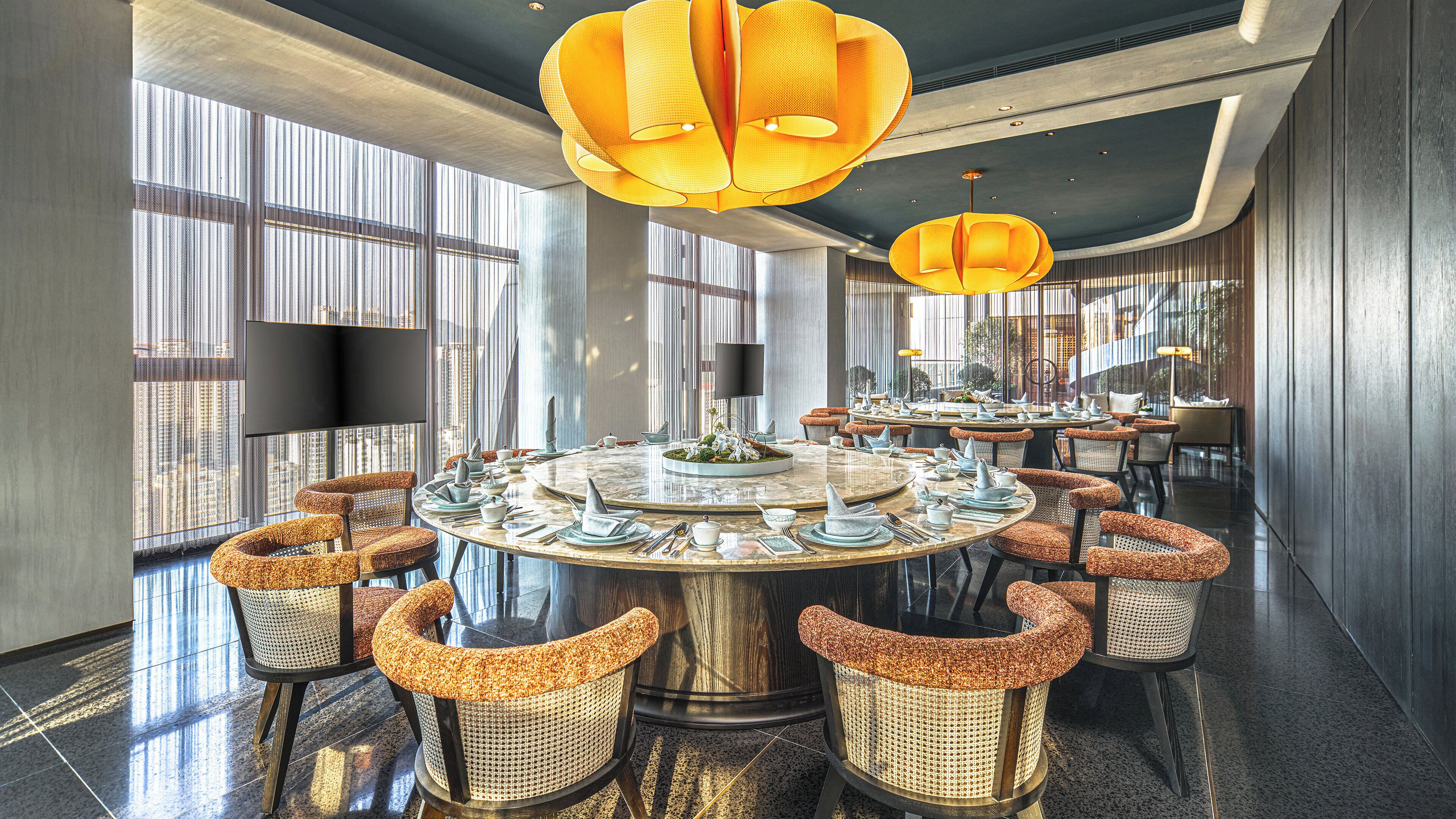 A modern dining area with round tables, wicker chairs, and a large chandelier.