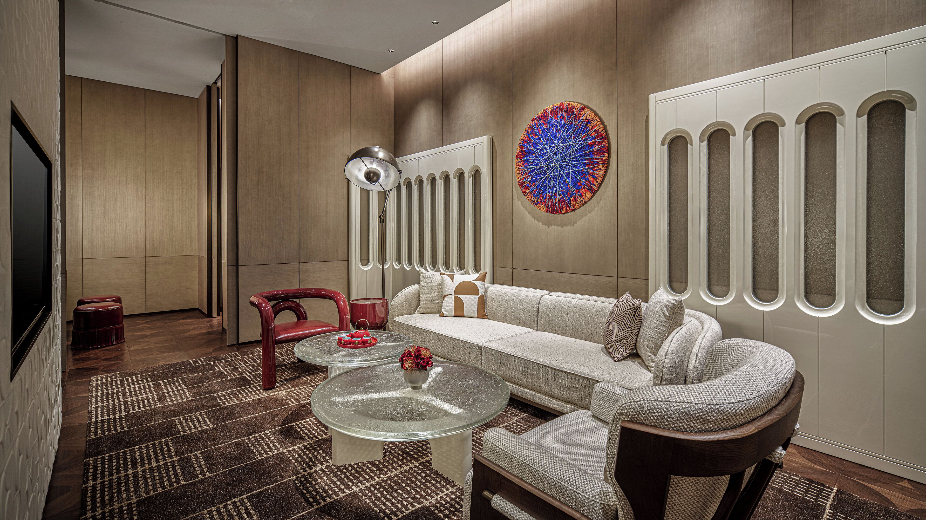 A modern living room with a sofa, two armchairs, a glass coffee table, and a patterned rug.