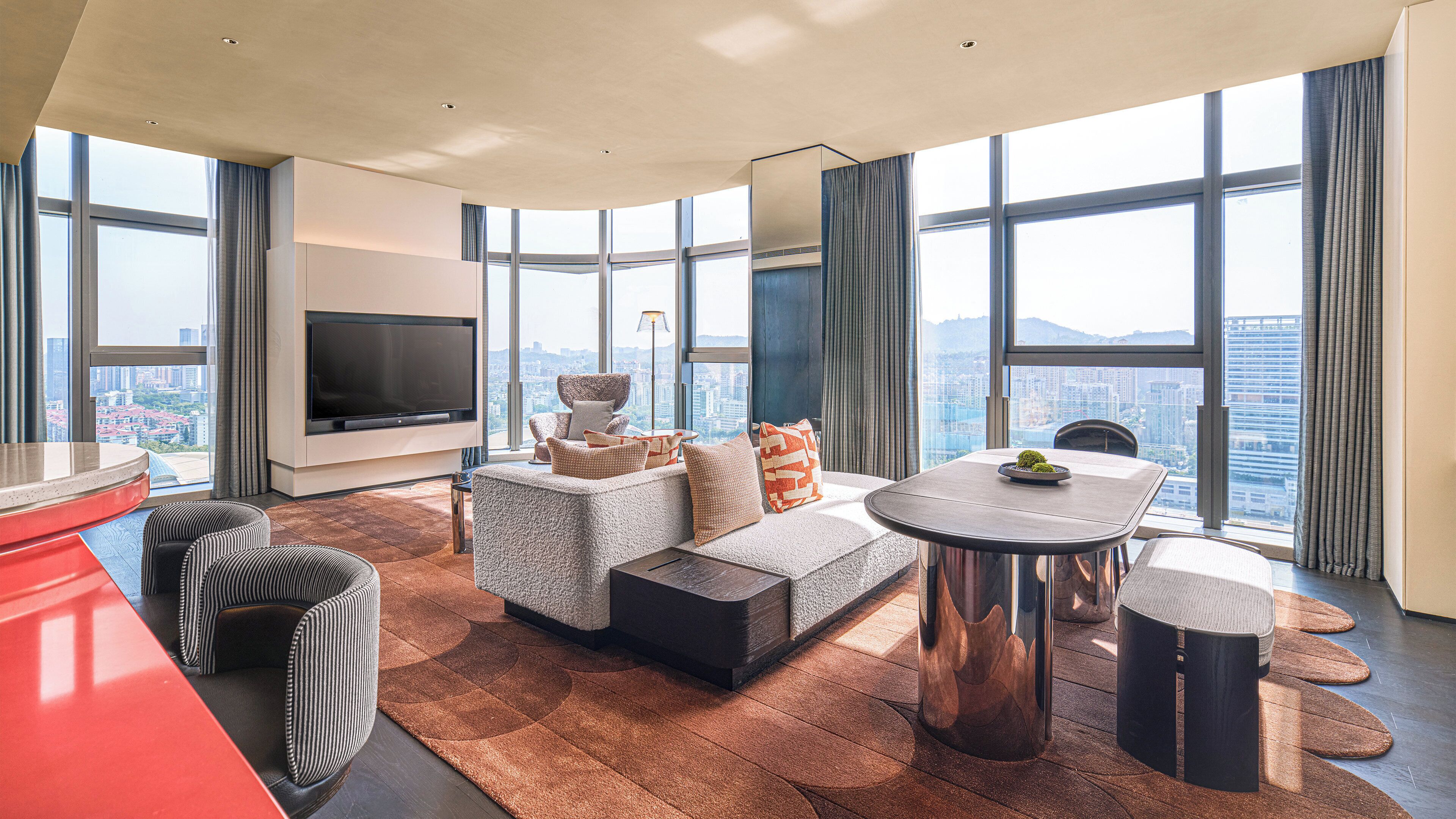 Una sala moderna con televisor de pantalla plana, un sofá, una mesa de centro y un comedor con vista a la ciudad.