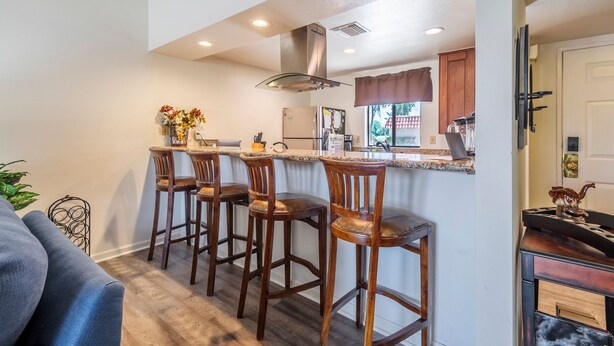 A kitchen with a bar area, wooden chairs, a refrigerator, and a window with a view.