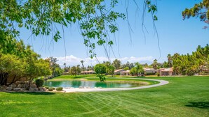 A well-maintained golf course with a pond, surrounded by lush greenery and residential buildings.
