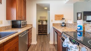 A kitchen with wooden cabinets, a microwave, a stove, a blender, and a sink.