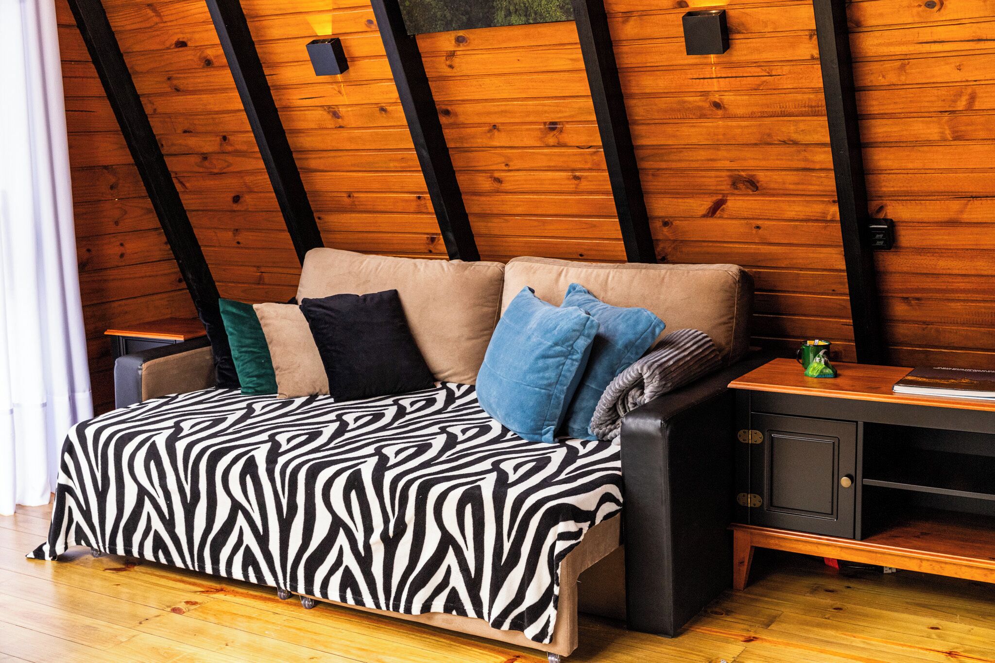 A cozy room with a zebra-patterned sofa, a wooden ceiling with exposed beams, and a small wooden side table.