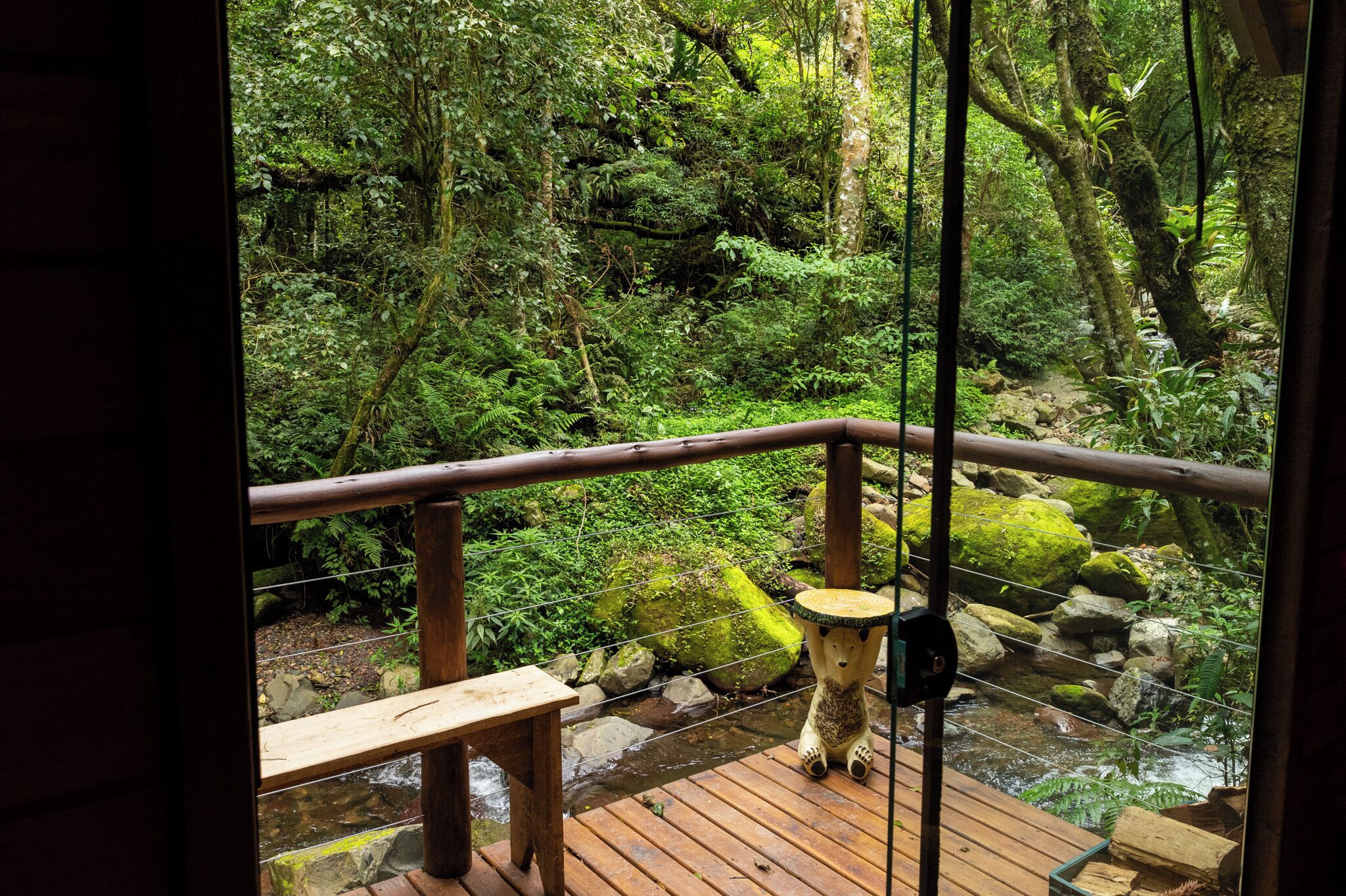 A wooden deck with a railing overlooking a forested area with a stream.