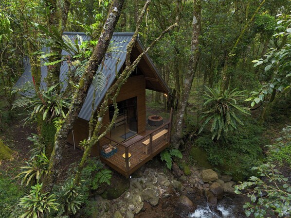 A wooden cabin with a balcony, surrounded by dense forest and a stream. - Refugio Soldados Sebold (Alfredo Wagner)