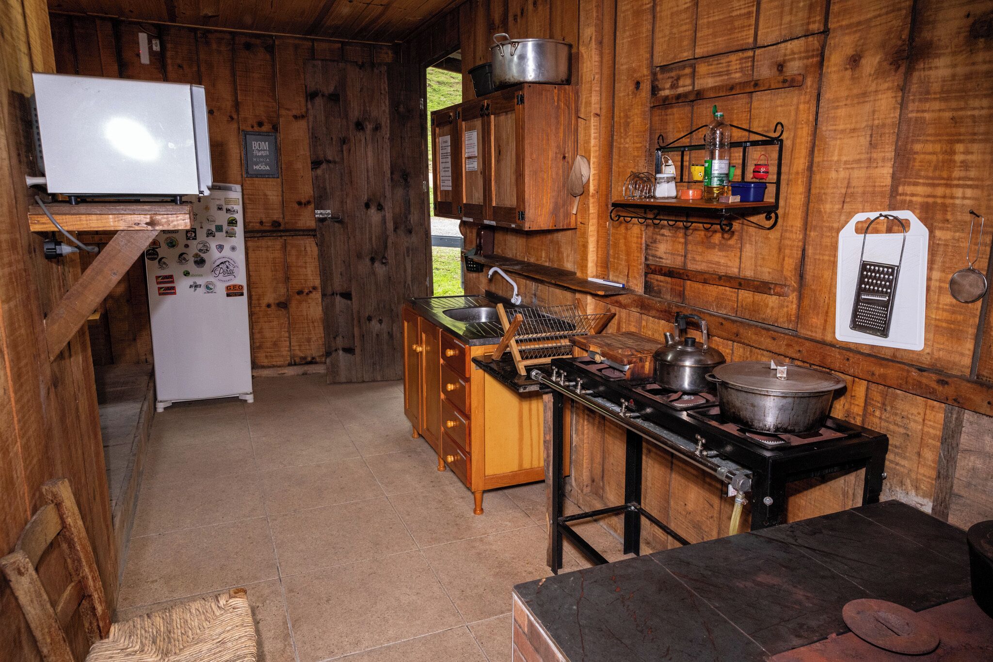 A rustic kitchen with wooden walls, a stove, a sink, and a refrigerator.