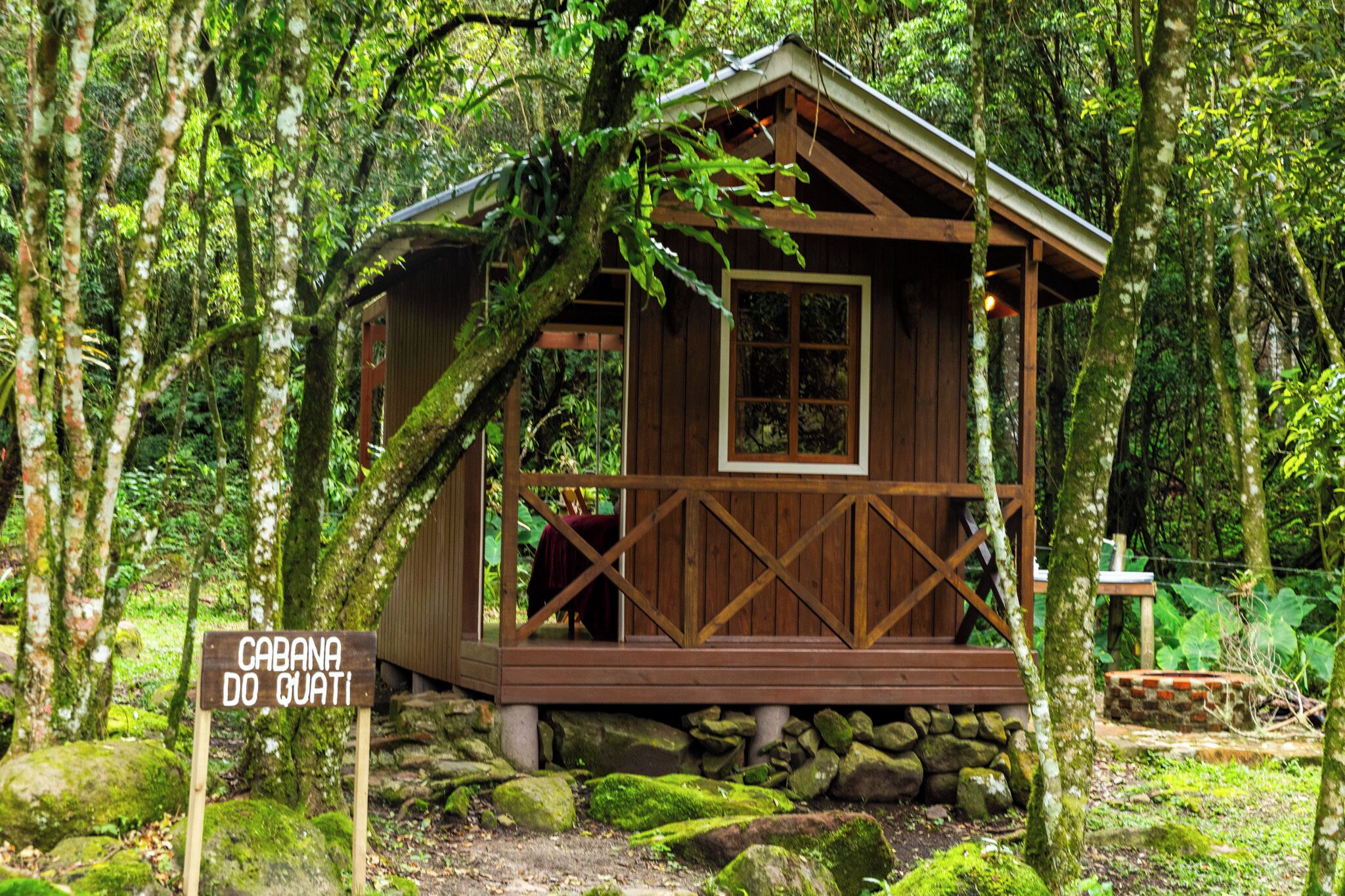 En stuga av trä, med namnet ”Cabana do Quati”, omgiven av en frodig skog.