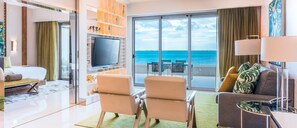 Une chambre d’hôtel avec un balcon, une télévision, un canapé et un coin repas avec des chaises.