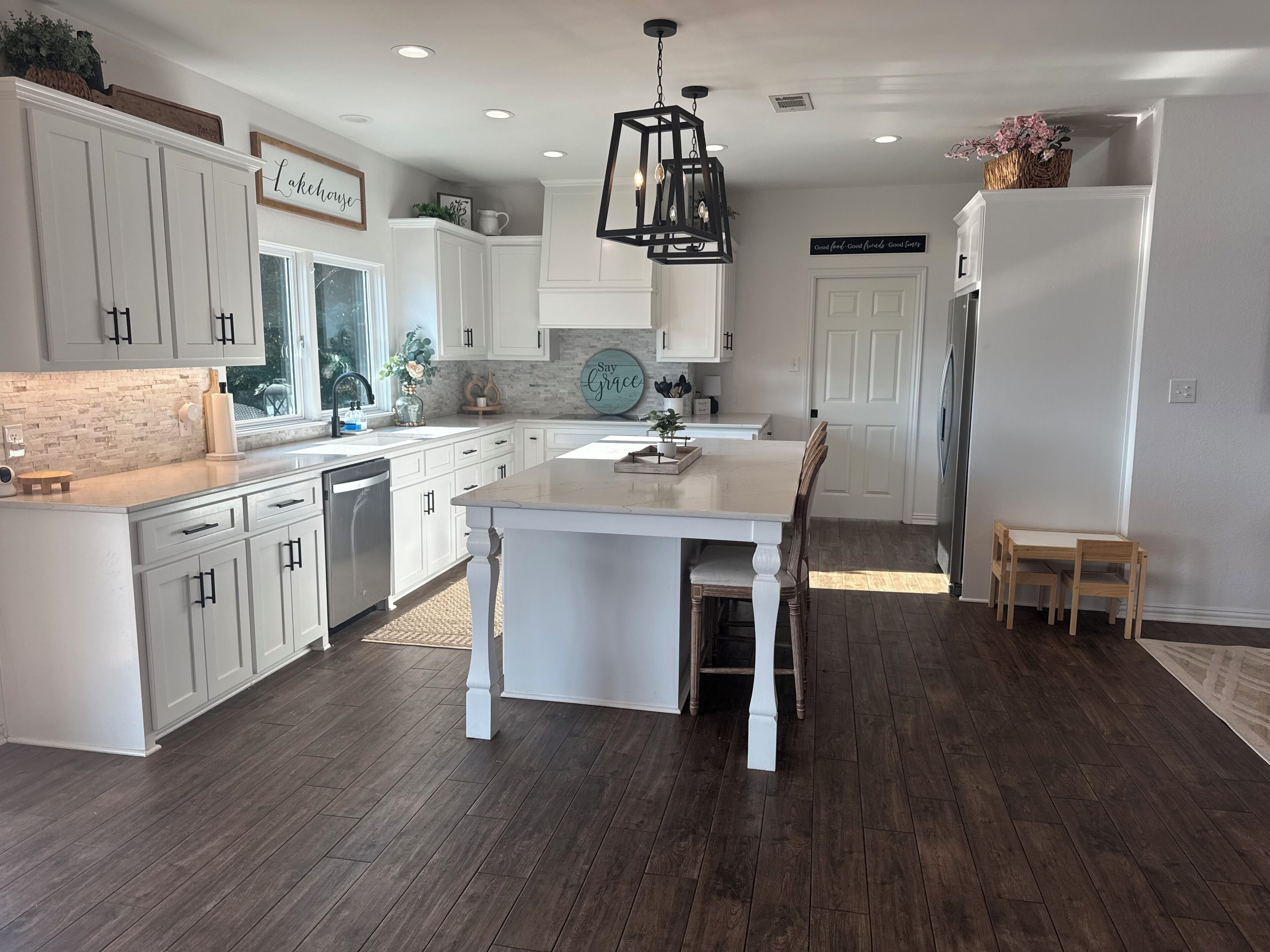 Une cuisine moderne avec des meubles blancs, un îlot central et un coin repas doté de chaises en bois.
