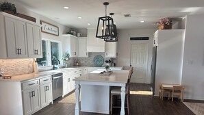 Een moderne keuken met witte kastjes, een centraal eiland en een eethoek met houten stoelen.