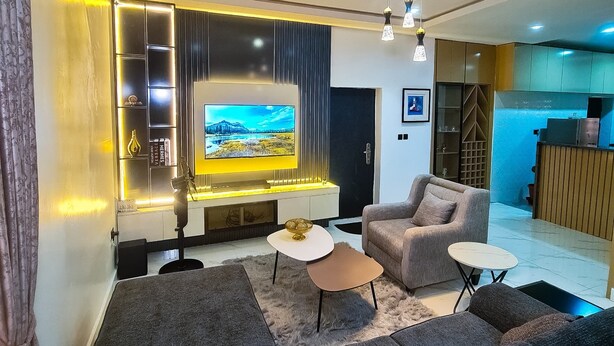 Una sala de estar moderna con un televisor de pantalla plana grande, un sofá, una mesa de centro y una cocina al fondo.