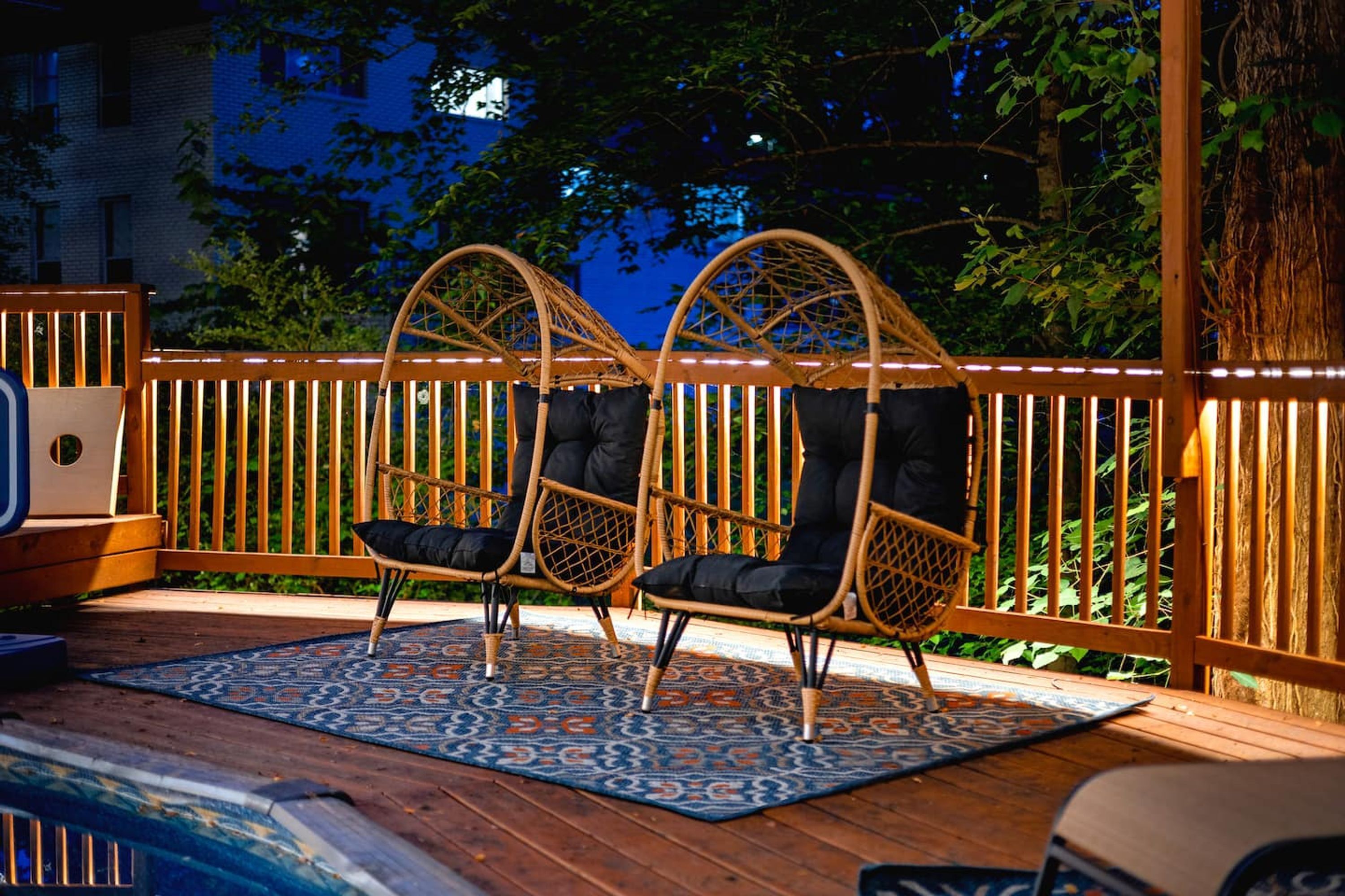 A deck with two wicker chairs, a patterned rug, and a wooden fence.