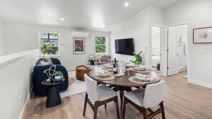 A modern living room with a dining area, featuring a round table set for six, a sofa, and a TV mounted on the wall. - Walkable 2BR Close to downtown, hiking, Red Rocks (Denver)