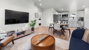 A modern living room with a flat-screen TV, a wooden coffee table, and a dining area with a table and chairs. - Walkable 2BR Close to downtown, hiking, Red Rocks (Denver)